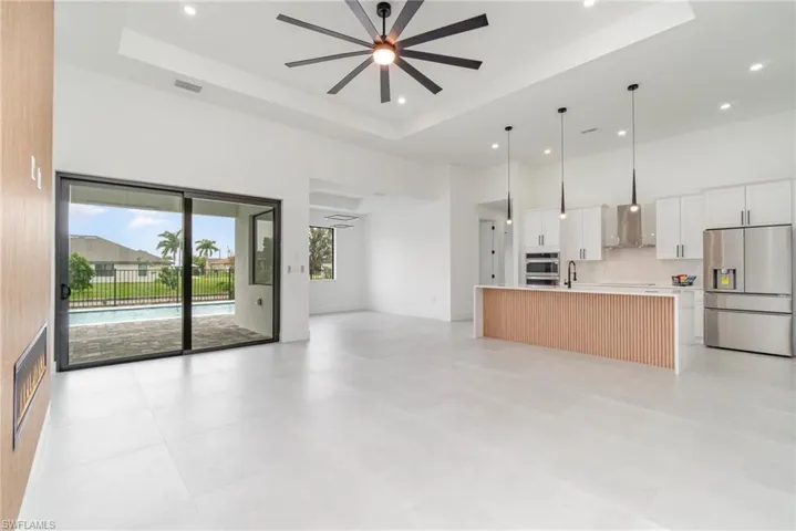 Unfurnished living room with light tile patterned flooring, a high ceiling, ceiling fan, and a raised ceiling