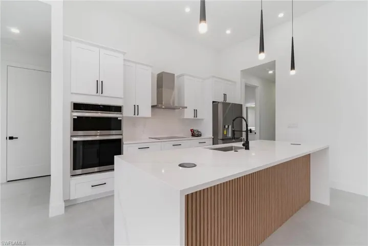 Kitchen featuring a center island with sink, stainless steel appliances, wall chimney exhaust hood, and white cabinets