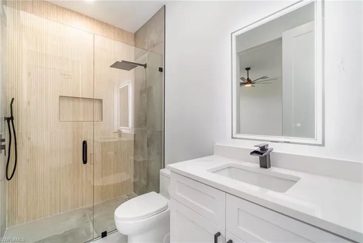 Bathroom featuring a shower with door, vanity, ceiling fan, and toilet