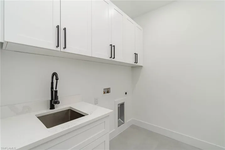 Laundry room with light tile patterned floors, hookup for a washing machine, cabinets, electric dryer hookup, and sink