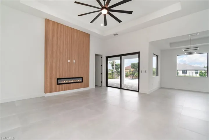 Unfurnished living room featuring a tray ceiling, a large fireplace, light tile patterned floors, and ceiling fan