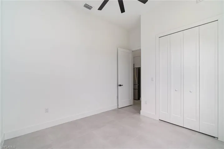 Unfurnished bedroom featuring light tile patterned flooring, a closet, stainless steel refrigerator, and ceiling fan