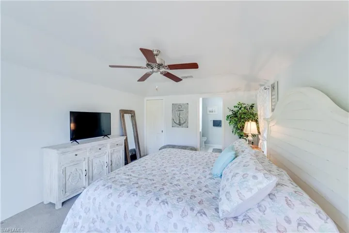 Bedroom with lofted ceiling, ceiling fan, light carpet, and connected bathroom