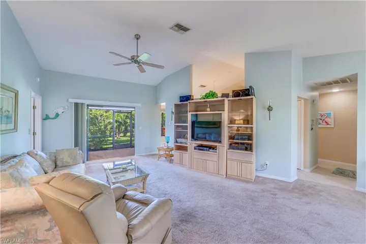 Living area featuring light colored carpet, ceiling fan, and vaulted ceiling