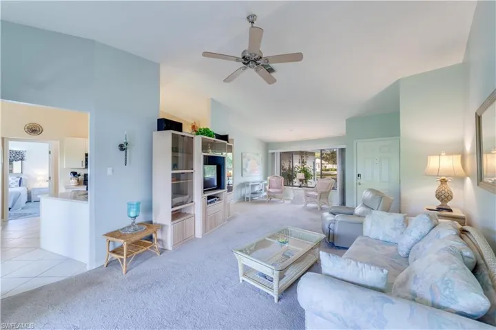 Living room featuring light colored carpet, ceiling fan, vaulted ceiling, and light tile patterned floors