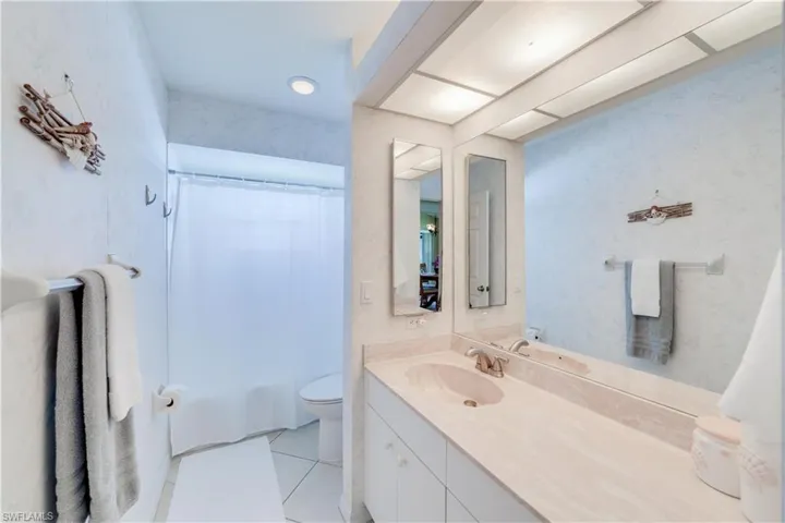 Bathroom with wallpapered walls, vanity, shower / bath combo with shower curtain, and light tile patterned floors