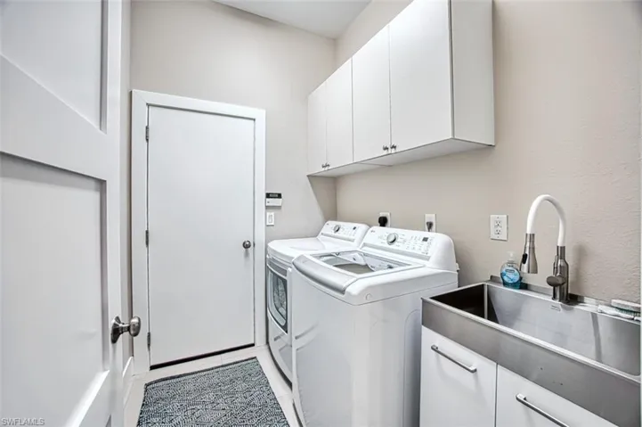 Clothes washing area with cabinets, independent washer and dryer, light tile patterned flooring, and sink