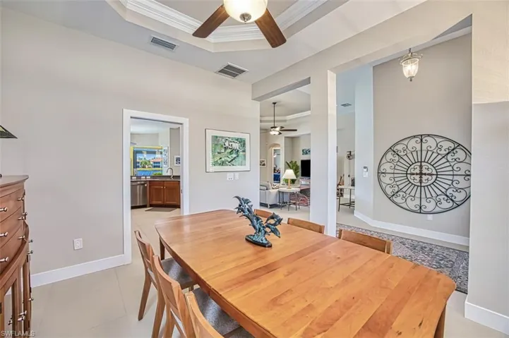 Dining space featuring sink, light tile patterned floors, ornamental molding, a raised ceiling, and ceiling fan
