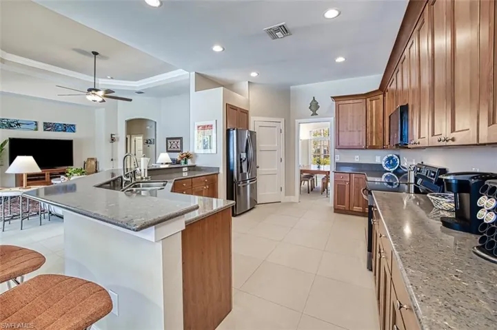 Kitchen with black electric range oven, light tile patterned floors, stainless steel fridge, and a breakfast bar area