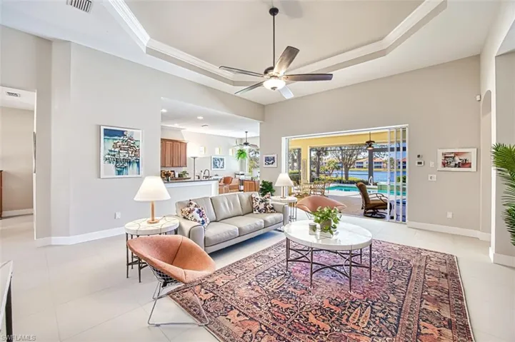 Tiled living room featuring crown molding, ceiling fan, a tray ceiling, and a towering ceiling