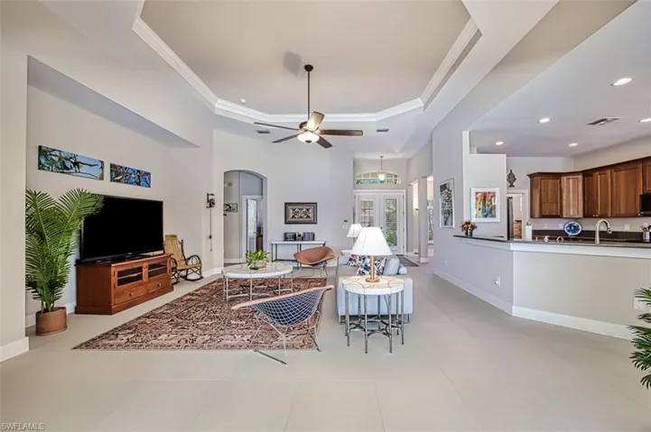 Living room featuring sink, light tile patterned floors, ornamental molding, a tray ceiling, and ceiling fan