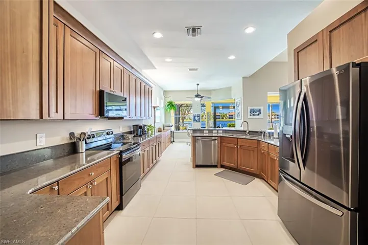Kitchen featuring sink, light tile patterned floors, stainless steel appliances, kitchen peninsula, and dark stone counters