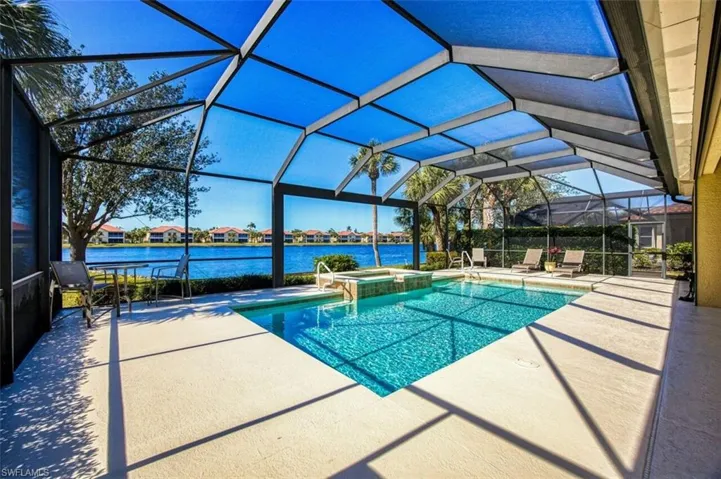 View of pool with an in ground hot tub, a water view, a patio area, and glass enclosure