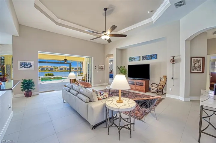 Tiled living room with a high ceiling, crown molding, ceiling fan, and a tray ceiling