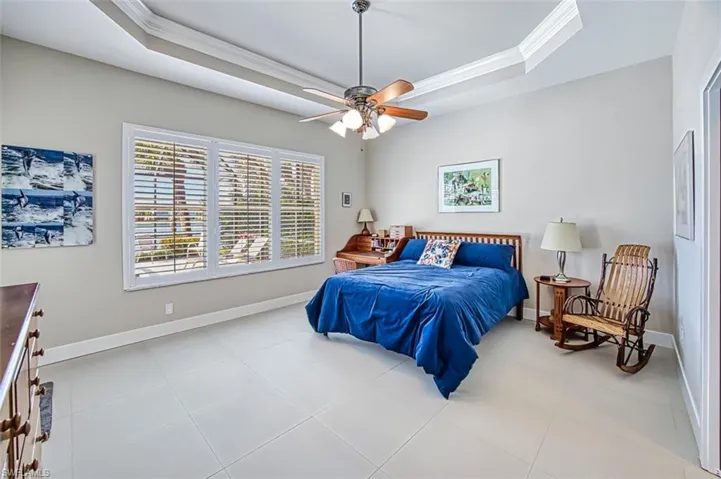 Tiled bedroom with ornamental molding, a raised ceiling, and ceiling fan
