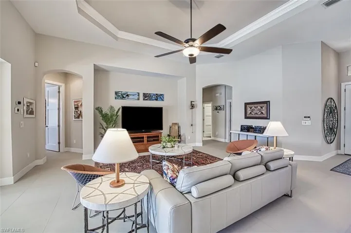 Living room with ornamental molding, light tile patterned floors, ceiling fan, and a tray ceiling