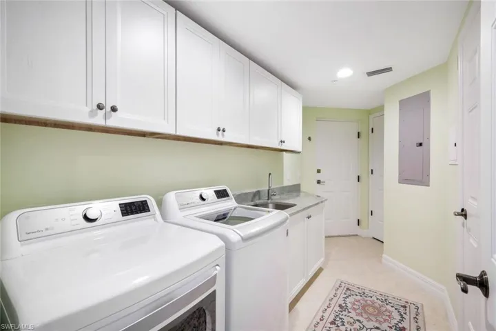Clothes washing area featuring cabinets, sink, light tile patterned floors, washing machine and clothes dryer, and electric panel