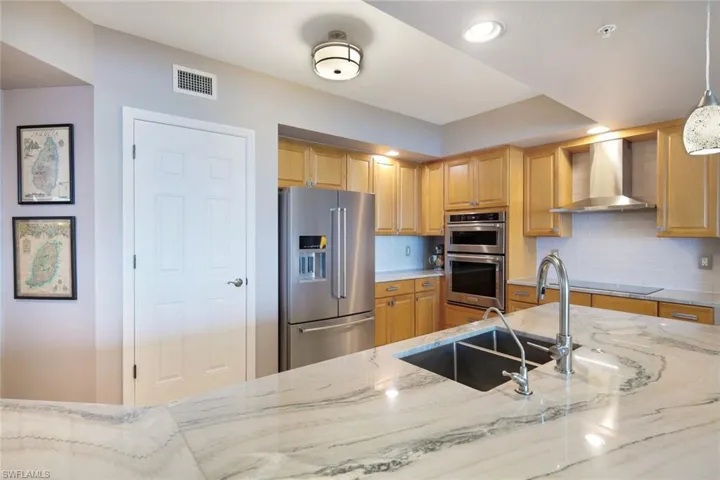 Kitchen with wall chimney exhaust hood, hanging light fixtures, tasteful backsplash, light stone counters, and appliances with stainless steel finishes