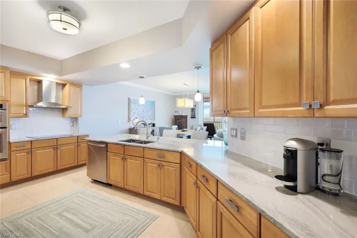 Kitchen featuring light stone countertops, sink, wall chimney exhaust hood, backsplash, and appliances with stainless steel finishes