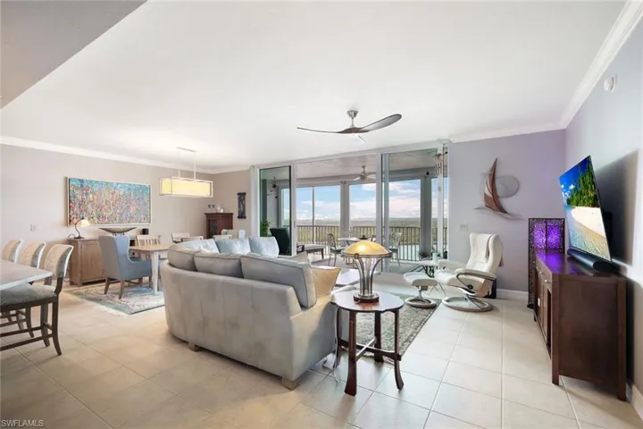 Living room featuring ceiling fan, expansive windows, light tile patterned flooring, and ornamental molding
