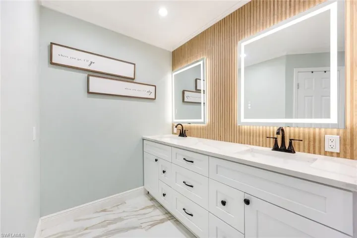 The primary bathroom features white shaker cabinets, quartz countertops and illuminated mirrors.
