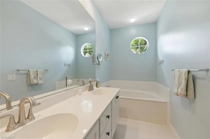 Full bath featuring a garden tub, double vanity, and light tile patterned floors