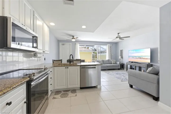 Kitchen with stainless steel appliances, a peninsula, dark stone countertops, white cabinets, and light tile patterned floors