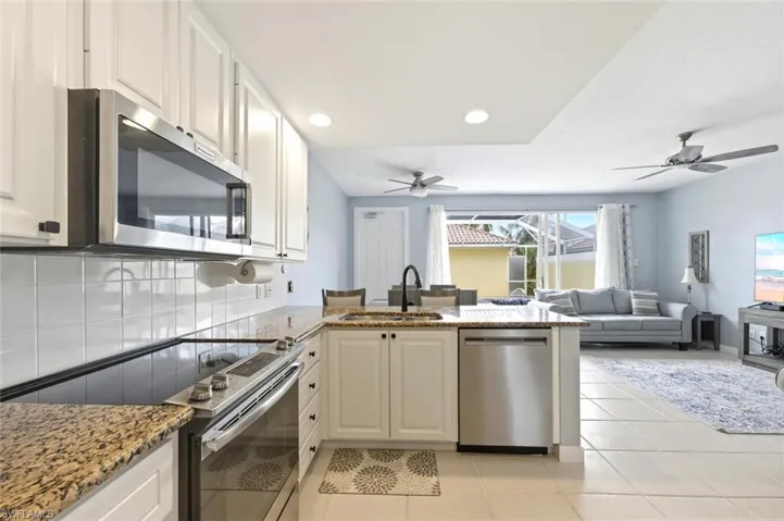 Kitchen with stainless steel appliances, a peninsula, light stone counters, ceiling fan, and open floor plan