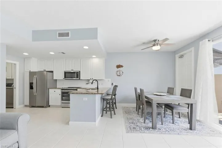 Kitchen with dark stone countertops, stainless steel appliances, white cabinets, ceiling fan, and a breakfast bar area