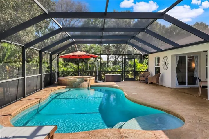 Screened-in outdoor living space featuring a freeform swimming pool, an integrated spa with stone-finish surround, and a spacious concrete patio