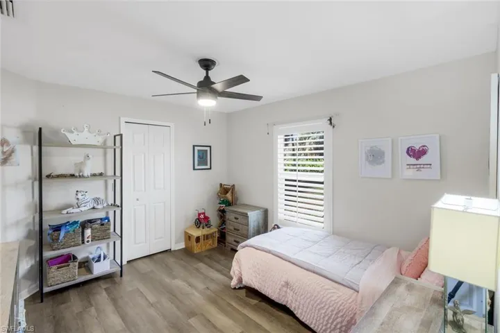 Bedroom featuring wood-finish flooring, a ceiling fan with integrated lighting, a window with plantation shutters, light-toned walls, and a bi-fold closet door