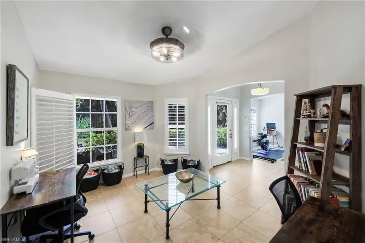 Bright room featuring tile flooring, multiple windows with white plantation shutters, a contemporary ceiling light fixture, and an arched doorway