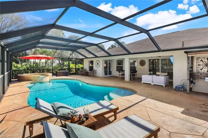 Screened outdoor living area featuring a freeform pool with integrated spa, expansive stamped concrete decking, and direct access to the interior