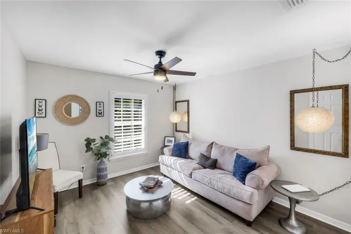 Living area featuring wood-finish flooring, a ceiling fan with integrated lighting, and a window with white plantation shutters