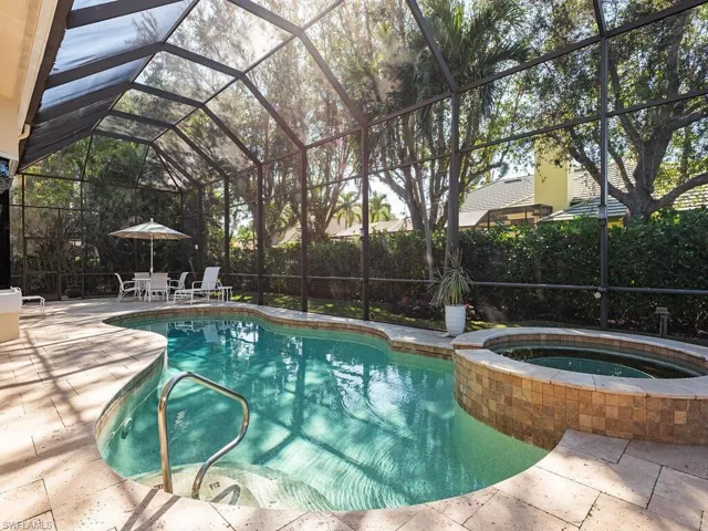 View of pool and in ground hot tub with screened lanai.