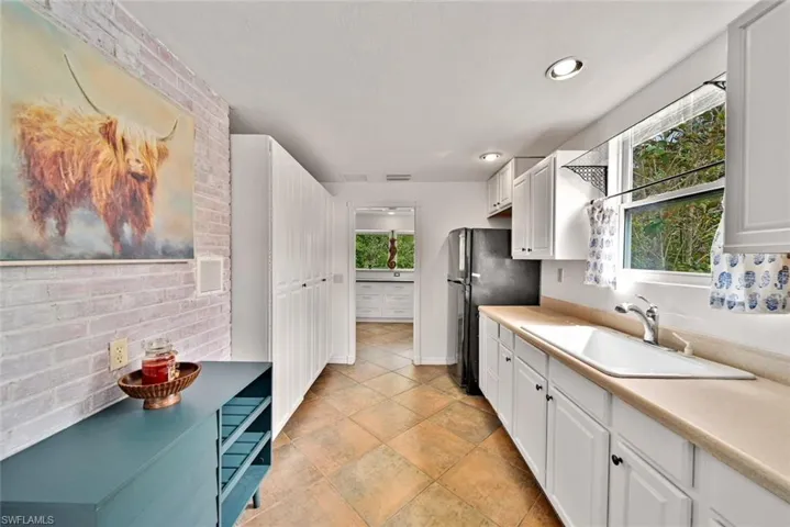 Kitchen featuring white cabinets, sink, backsplash, and black refrigerator
