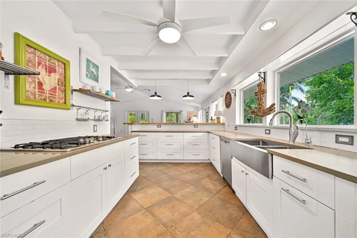 Kitchen with stainless steel appliances, white cabinetry, sink, tasteful backsplash, and lofted ceiling with beams
