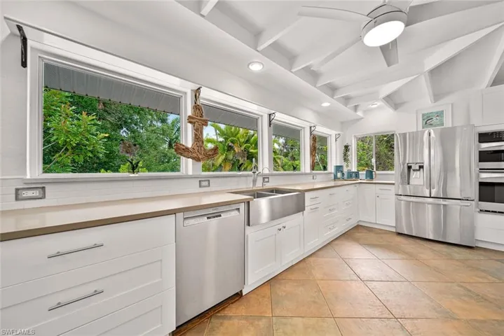 Kitchen featuring stainless steel appliances, decorative backsplash, sink, white cabinetry, and lofted ceiling with beams