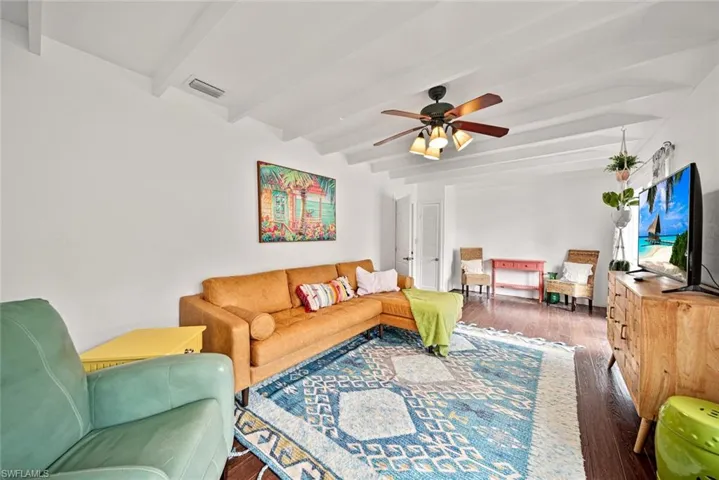 Living room featuring beamed ceiling, ceiling fan, and dark hardwood / wood-style floors