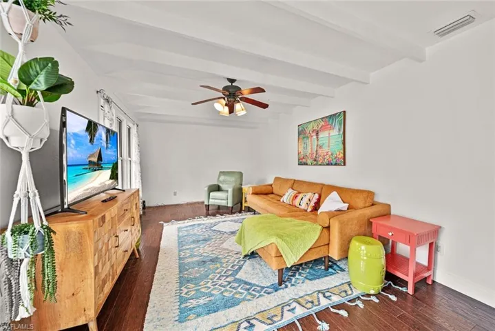 Living room with dark wood-type flooring, ceiling fan, and beam ceiling