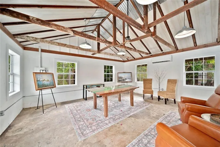 Recreation room with a healthy amount of sunlight, an AC wall unit, high vaulted ceiling, and beam ceiling