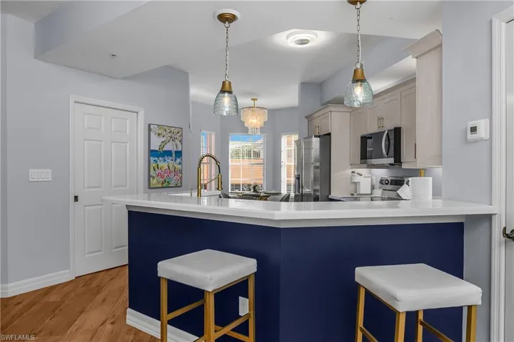 Kitchen with pendant lighting, a kitchen bar, stainless steel appliances, light wood-style floors, and a chandelier