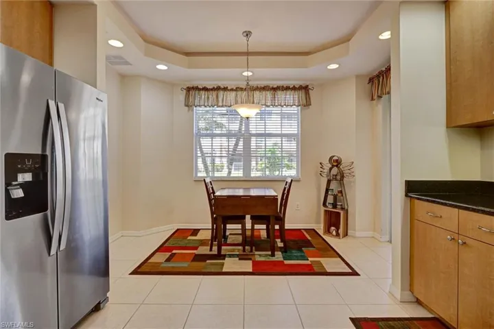 Bright dining area with recessed lighting, soaring raised tray ceiling, and light tile flooring