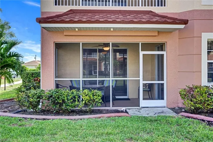 Exterior view of this Cape Coral condo entry showcasing stucco siding, tiled roof, screened lanai, and mature tropical landscaping