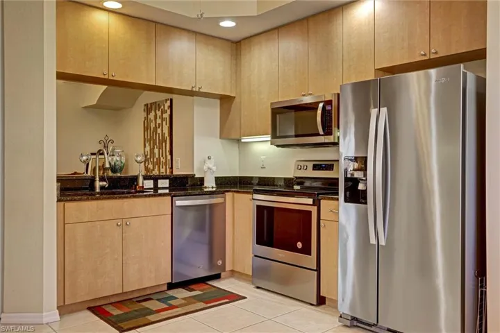 Well-appointed kitchen with stainless steel appliances, wood-tone cabinetry, dark stone counters, recessed lighting, and tile flooring