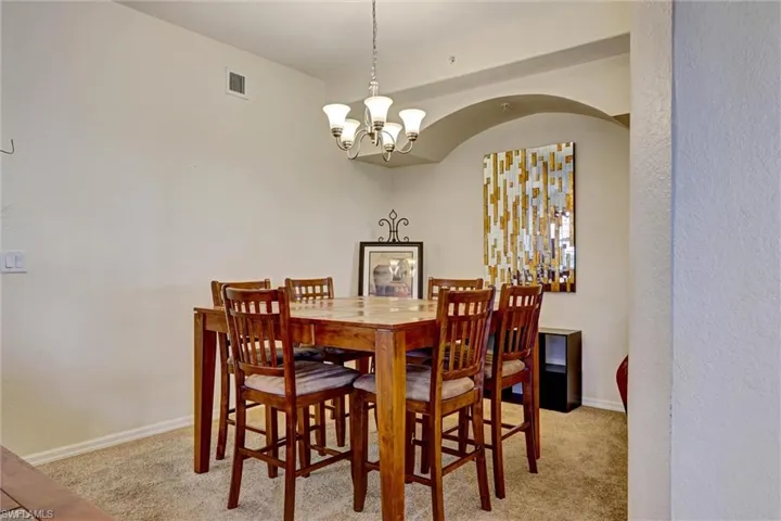 Dining space featuring chandelier, light-colored carpet, and tasteful textured accent wall