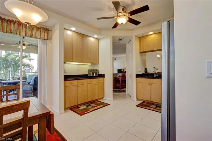 Functional kitchen with ceiling fan, full-size refrigerator, warm wood-tone cabinetry, and light tile flooring