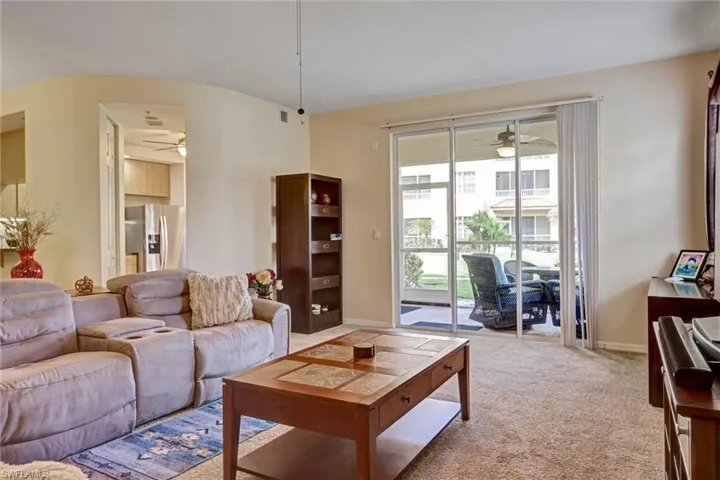 Open-concept carpeted living area with ceiling fan and graceful arched walkways — light-filled Florida living