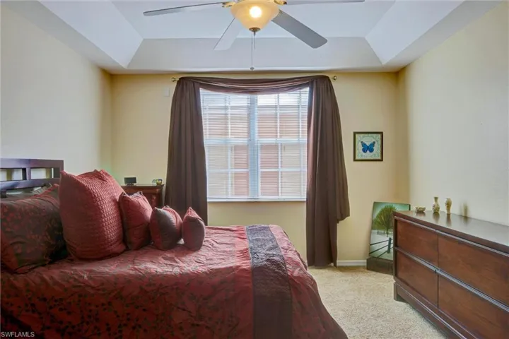 Spacious bedroom featuring an elegant tray ceiling, plush carpet, and ceiling fan