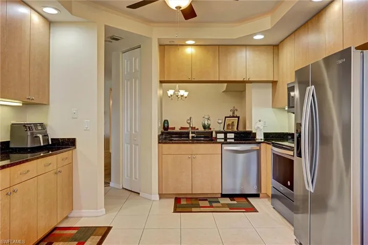 Updated kitchen with stainless steel appliances, dark granite-style countertops, ceiling fan, and warm wood-tone cabinetry